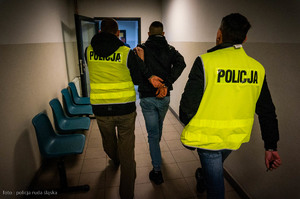 zdjęcie poglądowe z archiwum policji - dwóch policjantów prowadzi zatrzymanego mężczyznę korytarzem