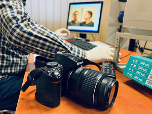 zdjęcie w pomieszczeniu technika kryminalistyki w trakcie wykonywania zdjęć do policyjnej bazy zatrzymanemu sprawcy - technik przy biurku, na komputerze widać fotografowanego sprawcę