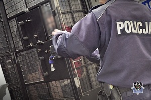 zdjęcie przedstawia policjanta przy tylnej części radiowozu przeznaczonej dla zatrzymanych - zamyka kratę