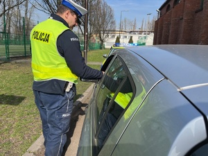 zdjęcie z policyjnych działań - policjant z drogówki stojący przy samochodzie osobowym, kierowca został ukarany mandatem za przekroczenie prędkości przy szkole