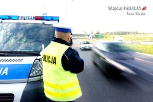 zdjęcie przedstawia policjanta kontrolującego prędkość, obok przejeżdża samochód osobowy