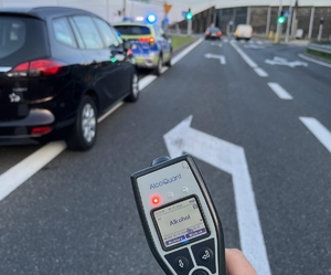 Alkomat w ręce policjanta, w tle kontrolowany samochód i radiowóz policyjny