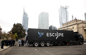 zdjęcie przedstawia samochód typu TIR z naczepą koloru czarnego stojący w centrum miasta, na boku duży napis ESCAPE - w tłumaczeniu UCIECZKA