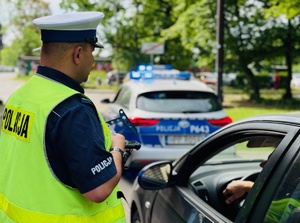 zdjęcie przedstawia policjanta drogówki w trakcie kontroli kierowcy osobówki