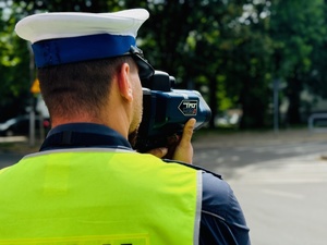 zdjęcie przedstawia policjanta z drogówki mierzącego prędkość pojazdów
