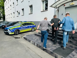 zdjęcie przedstawia policjantów prowadzących zatrzymanego do budynku komendy