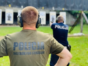 zdjęcie przedstawia zajęcia na strzelnicy otwartej podczas których instruktor przygląda się strzelającemu policjantowi