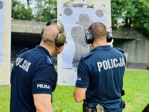 zdjęcie przedstawia zajęcia na strzelnicy otwartej podczas których instruktor i policjant strzelający oceniają wyniki na tarczy