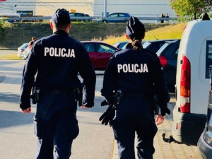 zdjęcie przedstawia policjantów idących wzdłuż parkingu z samochodami w pobliżu miejsca koncertów