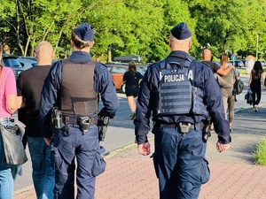 zdjęcie przedstawia policjantów idących chodnikiem w pobliżu bramy wejściowej na koncert