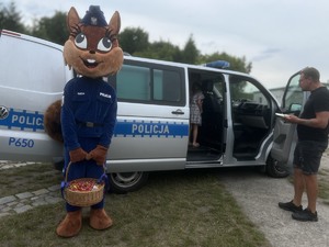 zdjęcie przedstawia maskotkę policji stojącą przy radiowozie