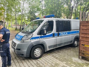 Na zdjęciu oznakowany radiowóz policji oraz policjant stojący bokiem do obiektywu