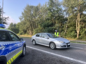 Na zdjęciu policyjny oznakowany radiowóz i umundurowany policjant, kontroluje trzeźwość kierujących