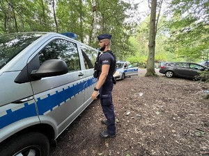 Na zdjęciu umundurowany policjant obok oznakowanego radiowozu