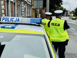 zdjęcie przedstawia policjantów z drogówki stojących przy policyjnym radiowozie w centrum miasta