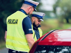 zdjęcie przedstawia policjantów z drogówki w trakcie kontroli kierowcy samochodu osobowego