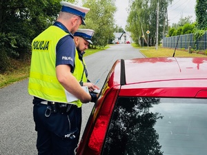 zdjęcie przedstawia policjantów z drogówki stojących przy kontrolowanym samochodzie osobowym