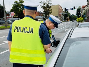 zdjęcie przedstawia policjantów z drogówki w trakcie kontroli związanej z przekroczeniem prędkości przez kierującego samochodem osobowym