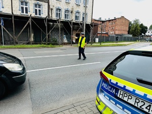 zdjęcie przedstawia policjanta z drogówki stojącego na drodze i zatrzymującego samochód do kontroli