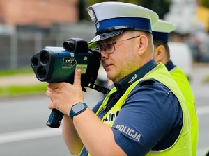 zdjęcie przedstawia policjanta z miernikiem prędkości dokonującego pomiar