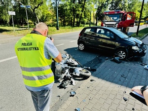 zdjęcie z miejsca wypadku - policyjny technik wykonuje zdjęcia miejsca wypadku, w tle widać rozbity samochód i motocykl