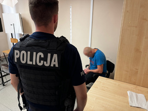 zdjęcie przedstawia policjanta z zatrzymanym w pomieszczeniu techników kryminalistyki