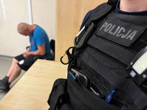 zdjęcie przedstawia policjanta z zatrzymanym w pomieszczeniu techników kryminalistyki