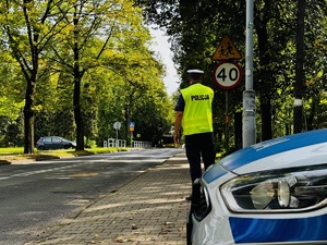 zdjęcie przedstawia policjanta z drogówki idącego w rejon przejścia dla pieszych przy szkole, widoczne są znaki ostrzegawcze charakterystyczne dla takiego przejścia