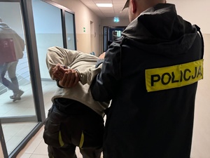 Policjant prowadzi sprawcę rozboju korytarzem komendy