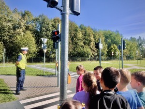 Dzieci wraz z umundurowanym policjantem w miasteczku ruchu drogowego, dzieci czekają na zielone światło dla pieszych