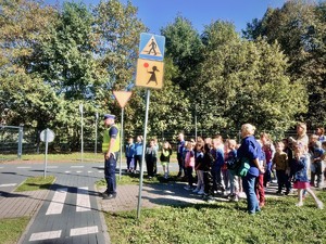 Dzieci wraz z umundurowanym policjantem w miasteczku ruchu drogowego, dzieci słuchają jak policjant omawia zasady