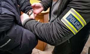 zdjęcie poglądowe przedstawia policjanta kryminalnego zakładającego kajdanki osobie zatrzymanej