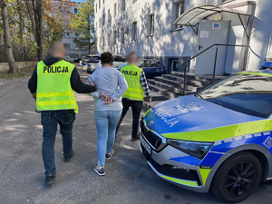 zdjęcie przedstawia policjantów prowadzących zatrzymaną przez parking przy komendzie