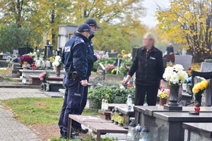 zdjęcie przedstawia policjantów na cmentarzu rozmawiających z seniorką sprzątającą grób