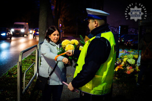 zdjęcie z akcji Świeć przykładem noś odblaski przedstawiające policjanta zakładającego na rękę kobiety odblaskową opaskę