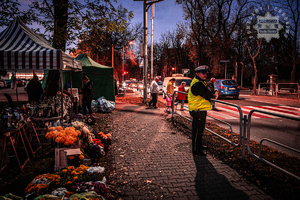 zdjęcie przedstawia policjanta z drogówki przy przejściu dla pieszych w rejonie cmentarza i straganów z kwiatami i zniczami