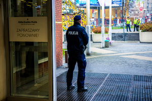 zdjęcie przedstawia policjanta pilnującego wejścia do centrum handlowego