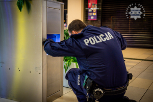 zdjęcie przedstawia pirotechnika sprawdzającego metalowy pojemnik stojący na pasażu centrum handlowego