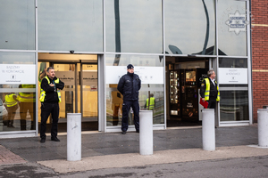 zdjęcie przedstawia policjanta i dwóch pracowników ochrony stojących przed wejściem do środka centrum