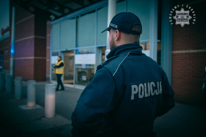 zdjęcie przedstawia policjanta stojącego przed wejściem do obiektu