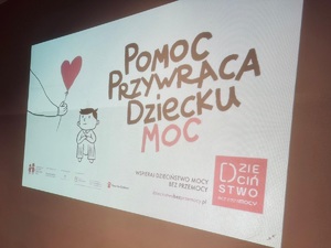 zdjęcie wyświetlanej na ścianie prezentacji z napisem pomoc daje dziecku moc, grafiką dziecka z balonem w kształcie serca