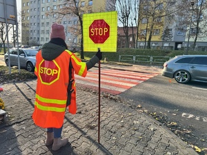 zdjęcie przedstawia pracownicę szkoły ze znakiem stop, potocznie zwaną &quot;Panią stopką&quot; w rejonie przejścia dla pieszych przy szkole podstawowej