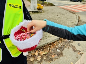 zdjęcie przedstawia policjanta z czapką mikołaja pełną cukierków i rękę kobiety sięgającej po słodycz