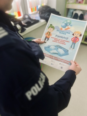 Na zdjęciu policjant trzyma plakat pod nazwą bezpieczna woda