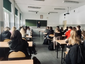 Uczniowie siedzący w szkolnych ławkach rozmawiają z policjantem