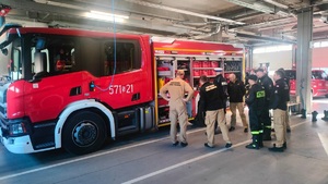 zdjęcie przedstawia wnętrze strażackiego garażu, strażaków i policjanta przy wozie bojowym