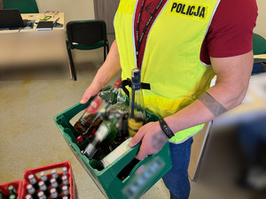 zdjęcie przedstawia policjanta trzymającego skrzynkę z piwem oraz butelki z alkoholem