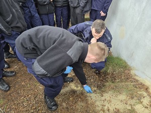 zdjęcie przedstawia policjanta i ucznia w trakcie odkopywania z pryzmy piasku granatu ćwiczebnego