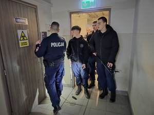 zdjęcie przedstawia policjanta pokazującego uczniom jak przeszukiwać pomieszczenia pod kątem ujawniania materiałów ywbuchowych