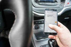 zdjęcie przedstawia wnętrze samochodu, a kierowca trzyma telefon w ręku i odpisuje na wiadomość
